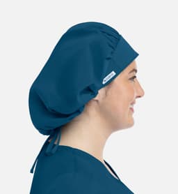 A unisex bouffant cap in deep teal, featuring a logo, worn by a model showcasing its profile.
