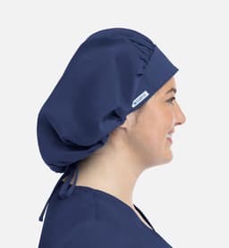 A unisex bouffant scrub cap in navy blue, worn by a model with a side profile. Features a logo.
