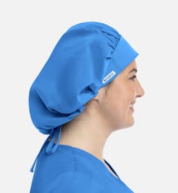 A unisex bouffant scrub cap in bright blue, worn by a model, with a logo tag visible on the side.