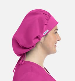 A unisex bouffant cap in vibrant pink, featuring a logo, worn on a person's head from the side.