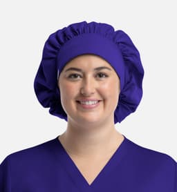 A unisex bouffant cap in purple, worn by a person with a smiling expression, featuring a soft, gathered design.
