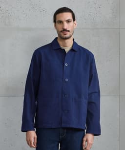 A navy blue chore jacket with a button-up front, featuring a simple design and a logo.