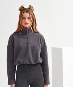 A grey cropped fleece top with a high collar and button detailing, paired with textured, high-waisted leggings.