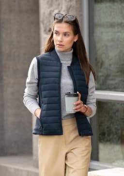 A navy women's vest with a lightweight design, paired with a grey turtleneck and beige pants, featuring a logo.