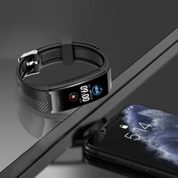 A black smart band with a digital display beside a smartphone, set on a reflective surface.