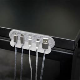 A cable organiser in grey holds multiple charging cables against a black surface. It features a fabric-like texture and a sleek design.