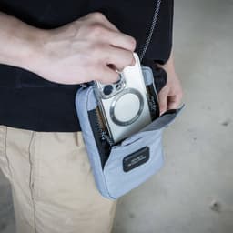 A grey eco-friendly bag with a phone being placed inside its front pocket, featuring a logo.