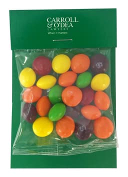 A clear bag containing multicoloured Skittles in yellow, green, red, purple, and orange hues, with a branded header.