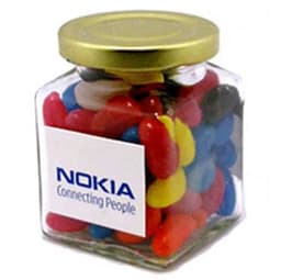 A glass square jar filled with colourful mini jelly beans, featuring a gold lid and a logo on the jar.