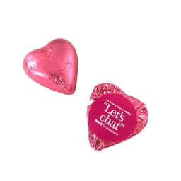 A pink chocolate heart wrapped in shiny foil, accompanied by a decorative foil wrapper with a logo.