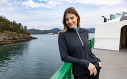 A half-zip hoodie in navy blue worn by a woman, featuring long sleeves and a subtle logo, against a scenic waterfront background.