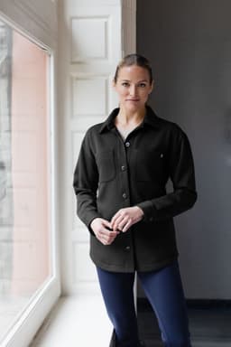A black eco shirt jacket with a button-up front and two chest pockets, worn by a model indoors.