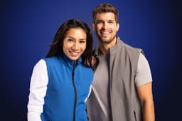 A blue vest and a grey vest are worn by a man and woman smiling together, set against a dark background.