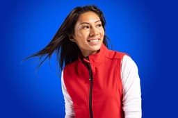 A woman wearing a red eco stretch vest with white sleeves, set against a blue background. The vest features a logo.