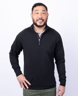 A man wearing a black half zip jumper with a collar and a logo on the chest.