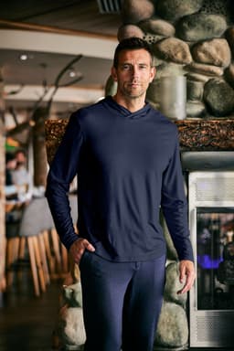 A men's hooded shirt in navy blue, featuring a relaxed fit and long sleeves, displayed indoors near a stone fireplace.