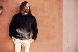 A black Stockholm hoodie displayed on a model against a warm-toned wall, featuring a front pocket and drawstring hood.