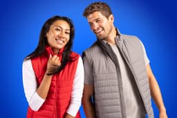A red and grey eco puffer vest worn by a man and a woman, both smiling against a blue background.