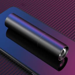 A sleek black torch lying on a reflective surface, showcasing its cylindrical design and shiny finish.