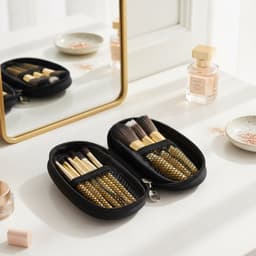 A black case containing nine makeup brushes with gold details, placed on a vanity beside a mirror and various beauty products.