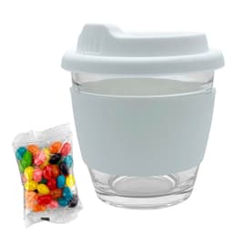 A reusable glass coffee cup in white with a silicone sleeve, accompanied by a bag of colourful jelly beans.