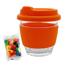 A glass coffee cup with an orange silicone lid and sleeve, accompanied by a pack of colourful jelly beans.