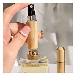 A mini bamboo atomiser held in a hand, with a perfume bottle in the background. The product features a natural bamboo finish.