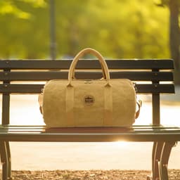 A kraft paper duffle bag in a tan colour sits on a park bench, featuring handles and a logo.