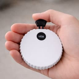 A drink bottle opener in white with a black toggle on top, held in a person's hand. Features a logo.