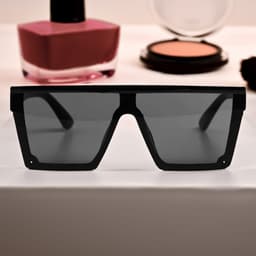 Black oversized sunglasses with dark lenses, displayed in front of cosmetics on a flat surface.