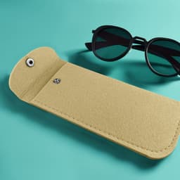 A yellow felt pouch lies on a teal surface next to a pair of black sunglasses, featuring a snap closure.