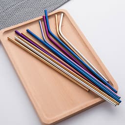 A wooden tray displaying various stainless steel drinking straws in vibrant colours, including gold, blue, purple, and silver.