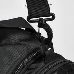 A close-up of a black duffle bag strap with a metal clip attachment. The bag has a textured surface.