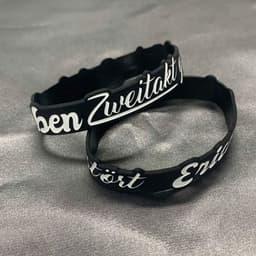 Two black silicone wristbands featuring white custom designs, displayed on a grey background.