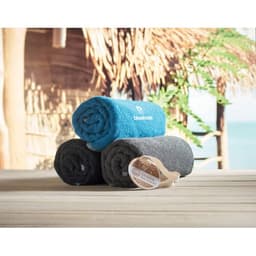 Three rolled towels in blue, grey, and black stacked on a wooden surface with a tropical background.