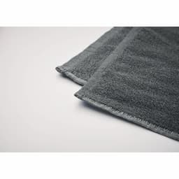 A dark grey towel with soft texture, featuring neatly stitched edges. It has a simple, elegant design.