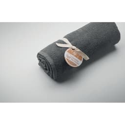 A rolled grey towel wrapped with a ribbon and a tag, resting on a light grey surface.