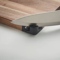 A cutting board with a wooden surface and a black corner piece, featuring a metal knife poised above it.
