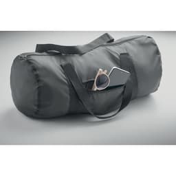 A black duffel bag featuring a phone and sunglasses in an exterior pocket. It has adjustable straps for carrying.