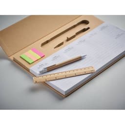 A stationery set featuring a notepad, ruler, pen, and pastel sticky notes in pink, green, and yellow. The set has a natural cardboard design.