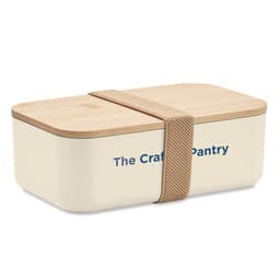 A cream-coloured lunch box with a bamboo lid and a fabric strap. The box features branding on the front.