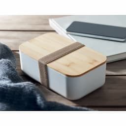 A bento box with a bamboo lid, featuring a white base and a brown strap, placed on a wooden surface.