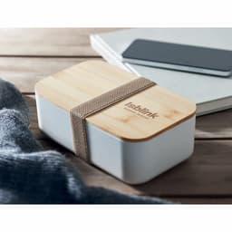 A food storage container with a white base and a wooden lid, secured by a beige strap, placed on a wooden surface.