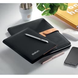 A black notebook with a leather cover, a silver pen, a white cup, and a yellow book on a tidy desk.