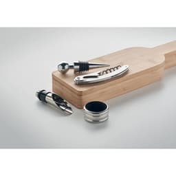 A wood serving board with a silver wine stopper, corkscrew, and pourer set displayed on top.