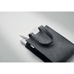 A grey felt tote bag with handles, holding a notepad and pens, featuring a logo.
