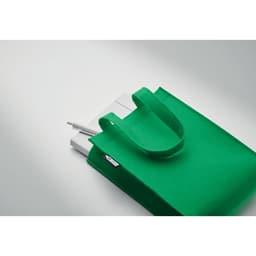 A green tote bag containing white items, including pens. The bag has a logo and two sturdy handles.