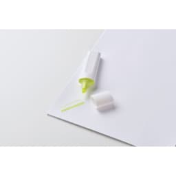 A highlighter in white casing with a bright green tip sits on a blank piece of paper, with a few lines drawn next to it.
