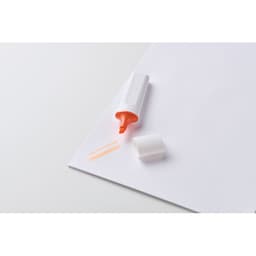 A highlighter in white and orange, with a cap removed, resting on a sheet of paper alongside two orange lines.