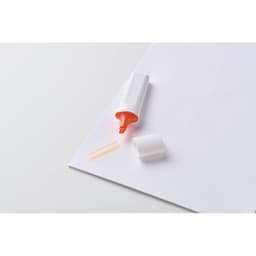 A highlighter in orange colour, lying on a white sheet of paper, with the cap beside it.